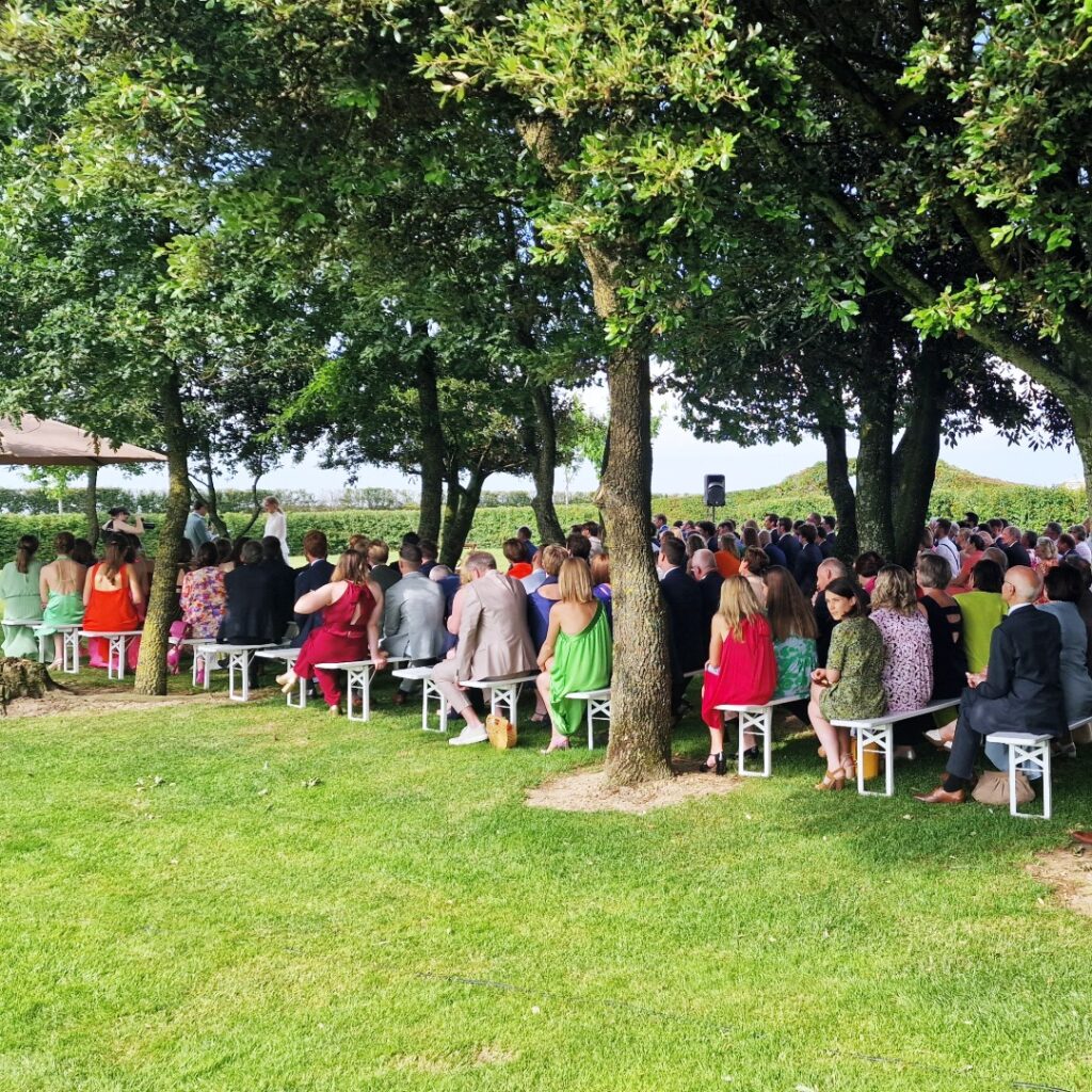 Buiten ceremonie onder de bomen bij ’t Convent met gasten op witte banken.